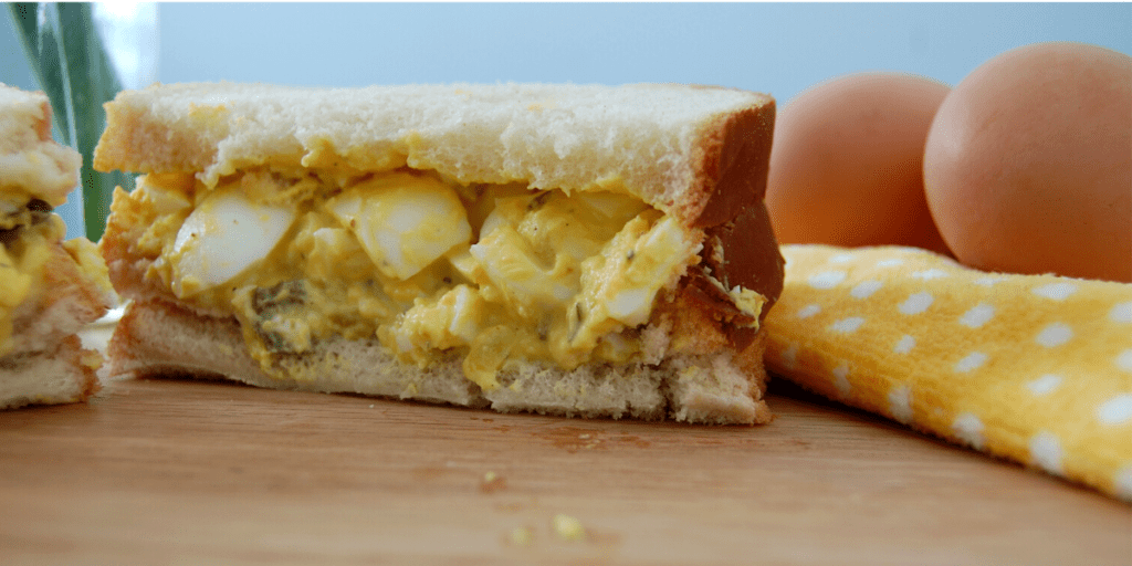 half an egg salad sandwich on a cutting board beside some hard boiled eggs