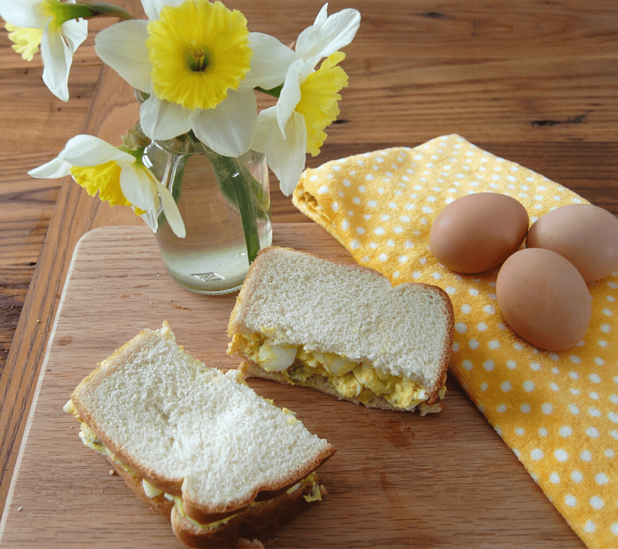 egg salad sandwich cut in half on a cutting board beside three boiled eggs 