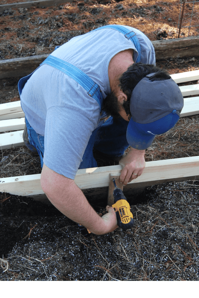 man attaching new supports to side of raised bed using cordless drill to adjust its height