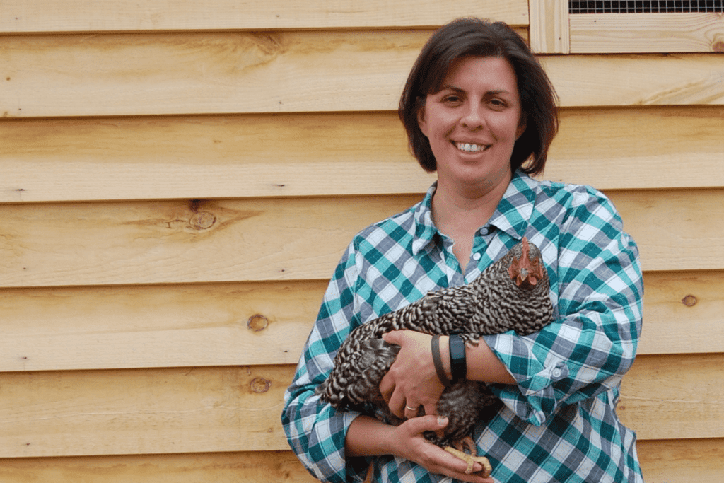 woman holding chicken in front of chicken coop