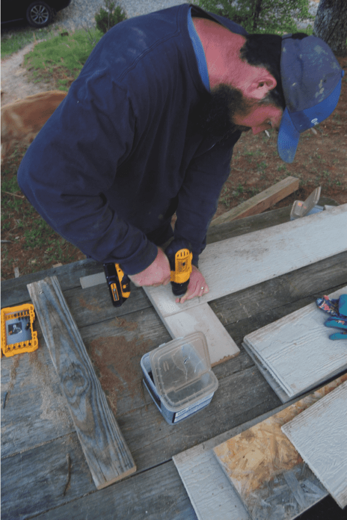 man using a cordless drill to attach supports to the sides of a raised garden bed