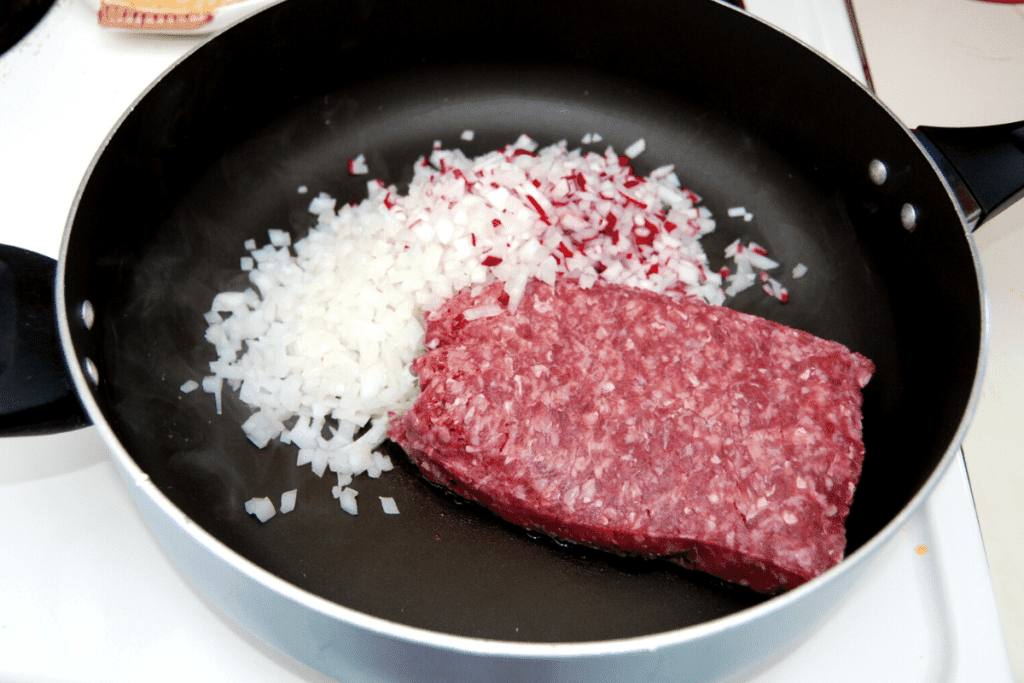 skillet with ground beef, diced onions, and diced radishes on the stove
