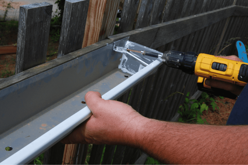 close up of hands drilling a hidden gutter hanger into a gutter and fence post
