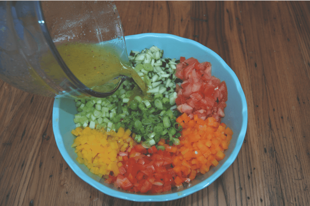 pouring dressing from a measuring bowl into a bowl of fresh diced vegetables