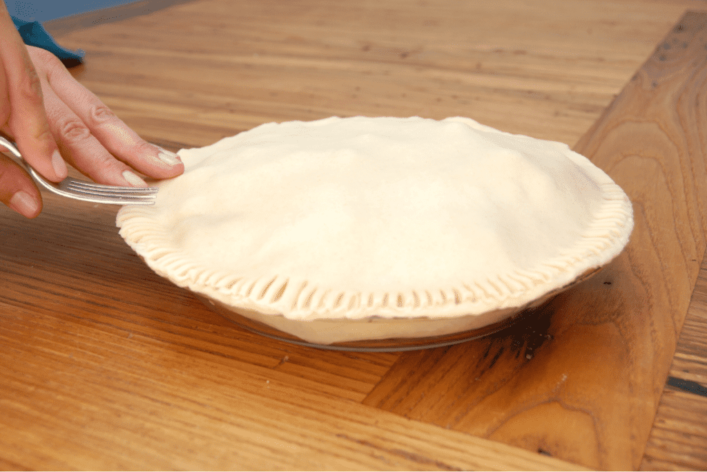 close up of hands using a fork to crimp and seal the edges of the pie crust for the fresh blackberry pie