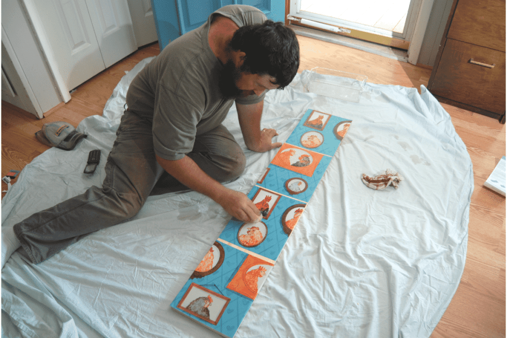 man wiping down chicken print wallpaper with a sponge on a wooden board