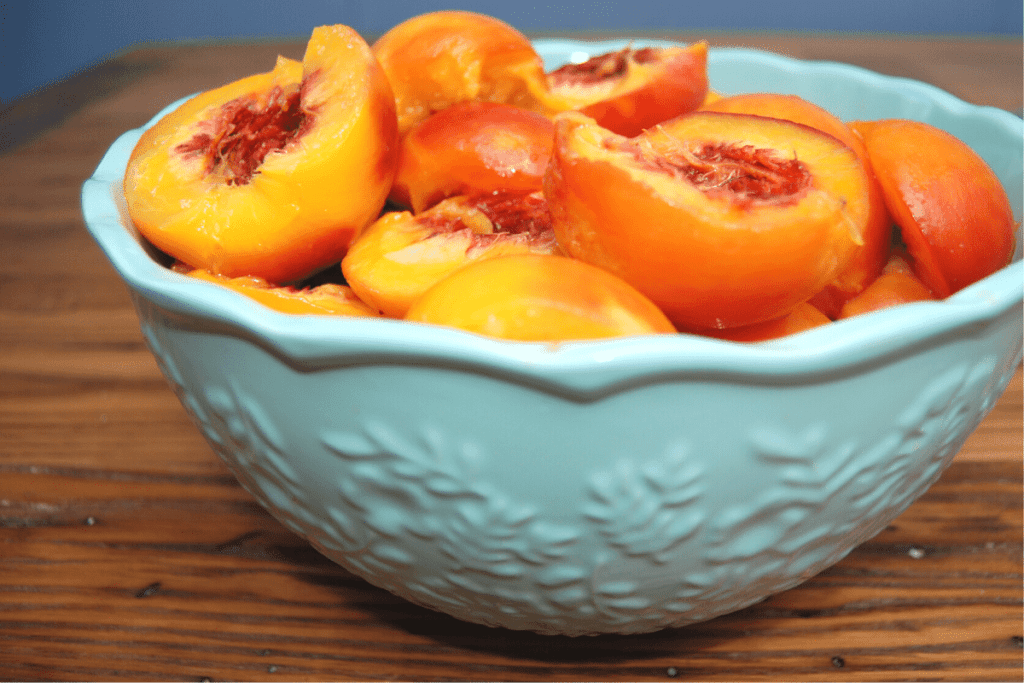 peaches peeled and halved in a bowl on a table ready for fresh peach ice cream
