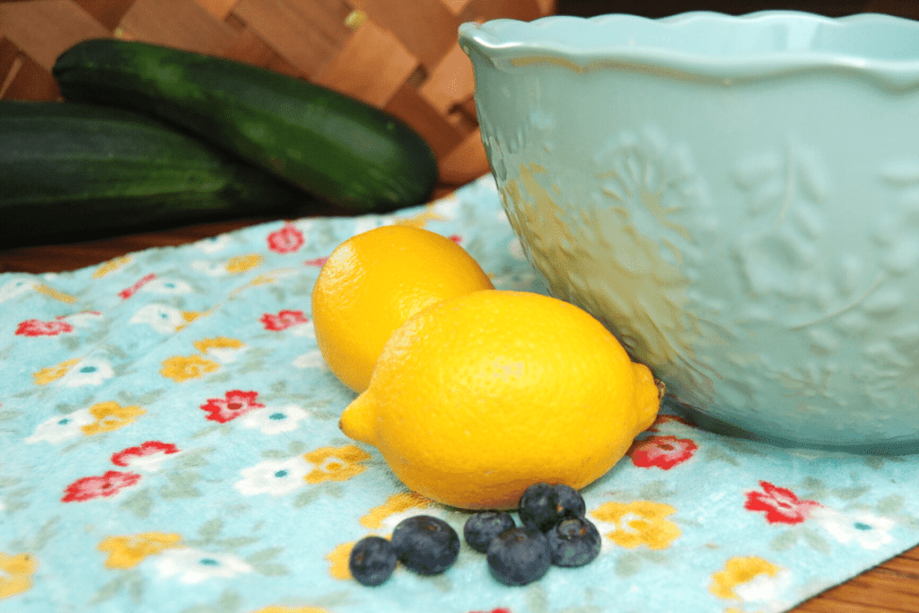 zucchini, lemons, blueberries, a bowl and a kitchen towel on a table