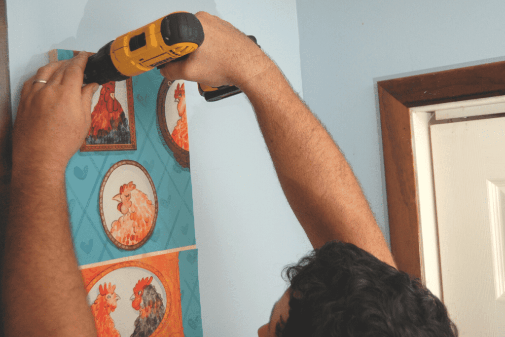 man using an electric drill to attach wooden board to the wall for egg storage