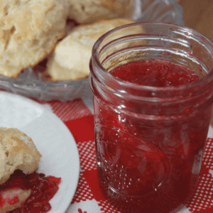 close up of a jar of strawberry jam and a plate with a biscuits