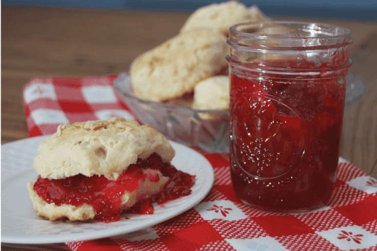 jar of strawberry jam beside a biscuit on a plate